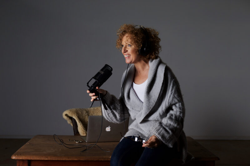Woman sitting on desk holding a podcast microphone