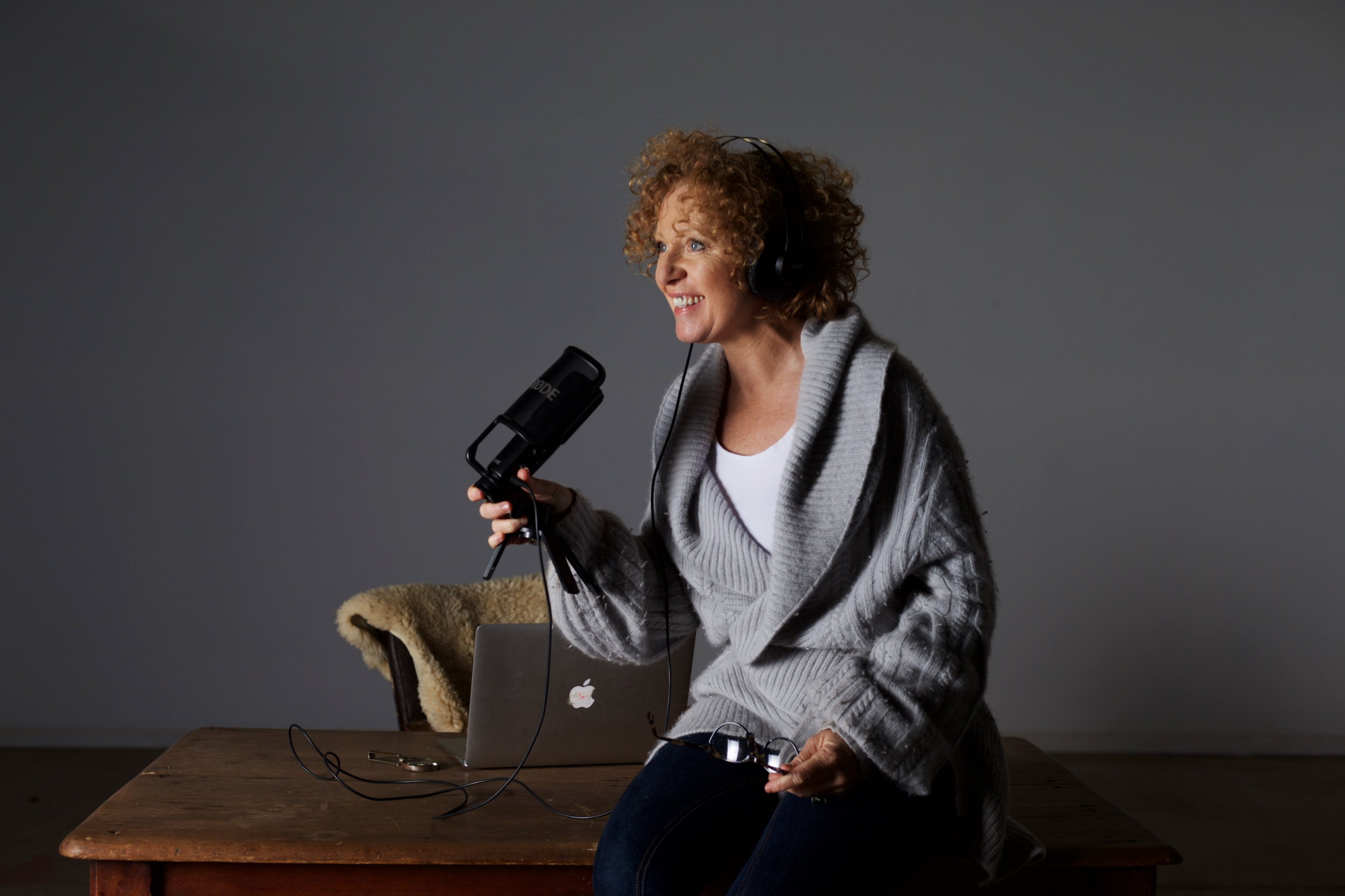 Woman sits on desk with a podcasting microphone