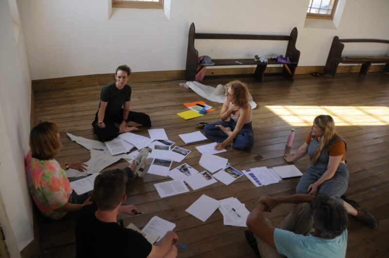 Group of people sitting in a circle surrounded by paper